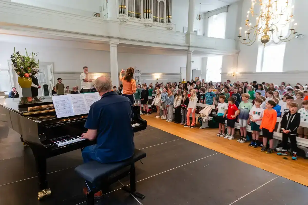 Kinderkoor zingt met dirigent en pianist in de Grote Kerkzaal tijdens het Internationaal Lied Festival Zeist