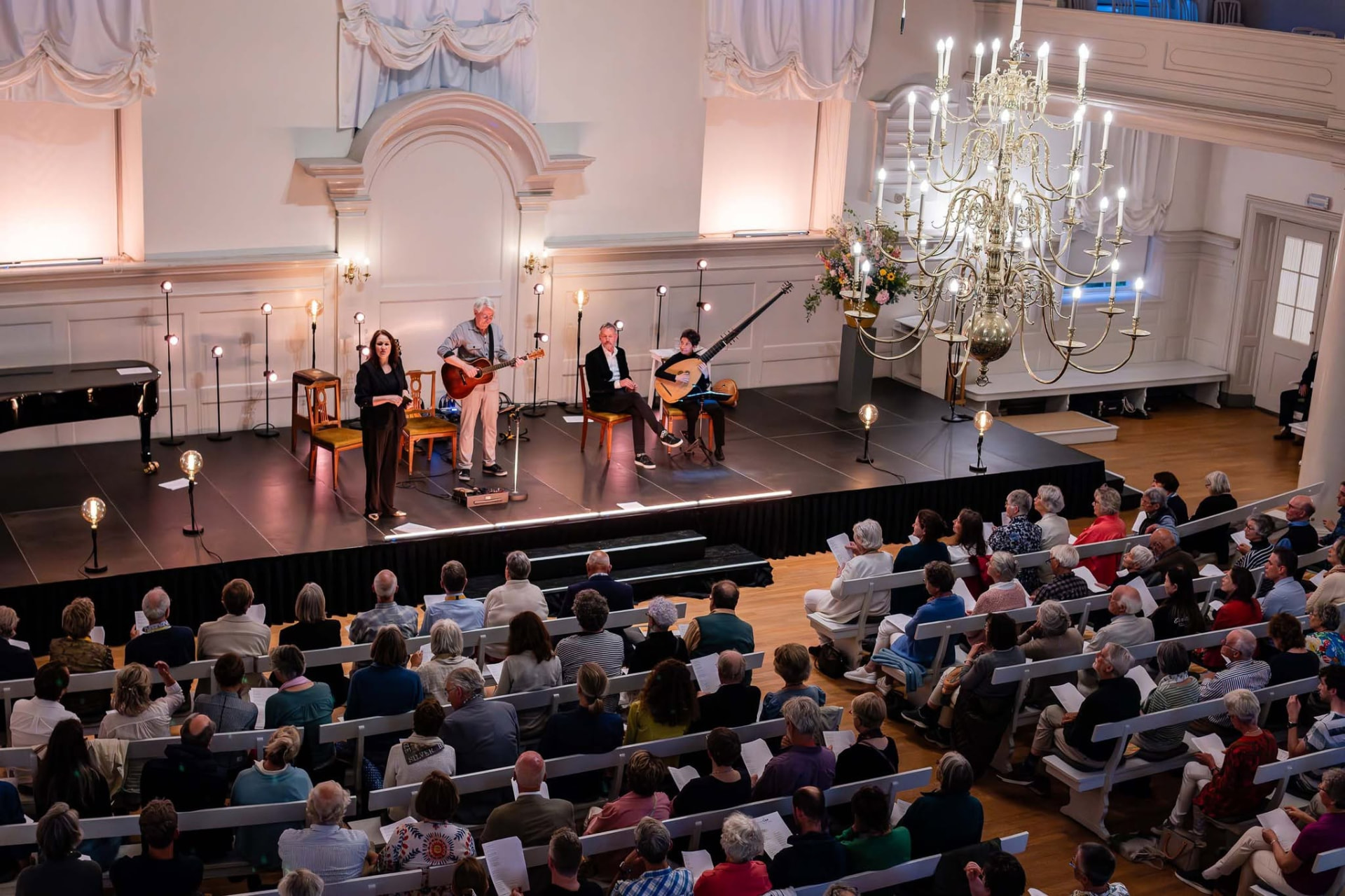 Concert met publiek in de lichte kerkzaal met kroonluchter