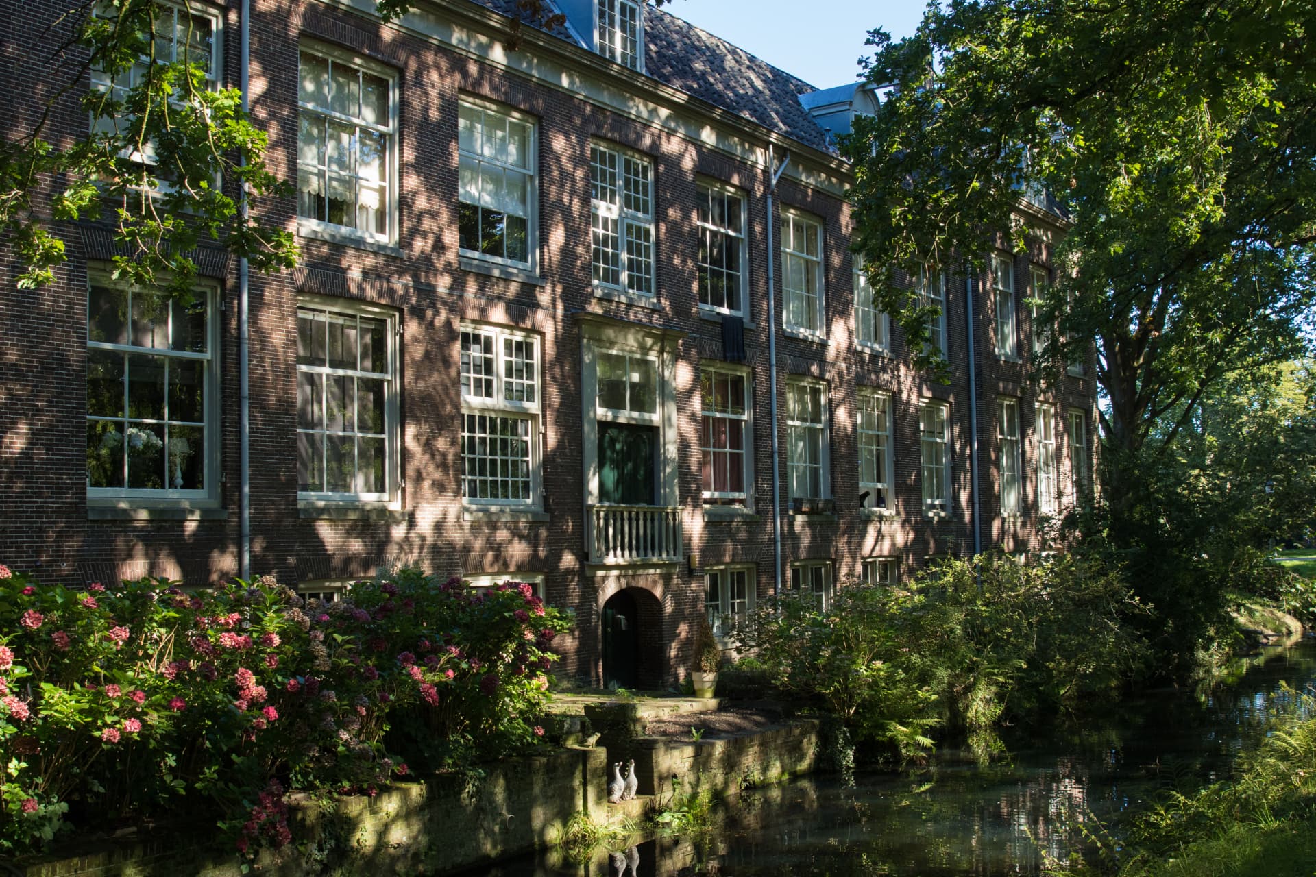 Monumentaal pand met woningen en werkruimten aan het water, met hortensia's langs de gracht
