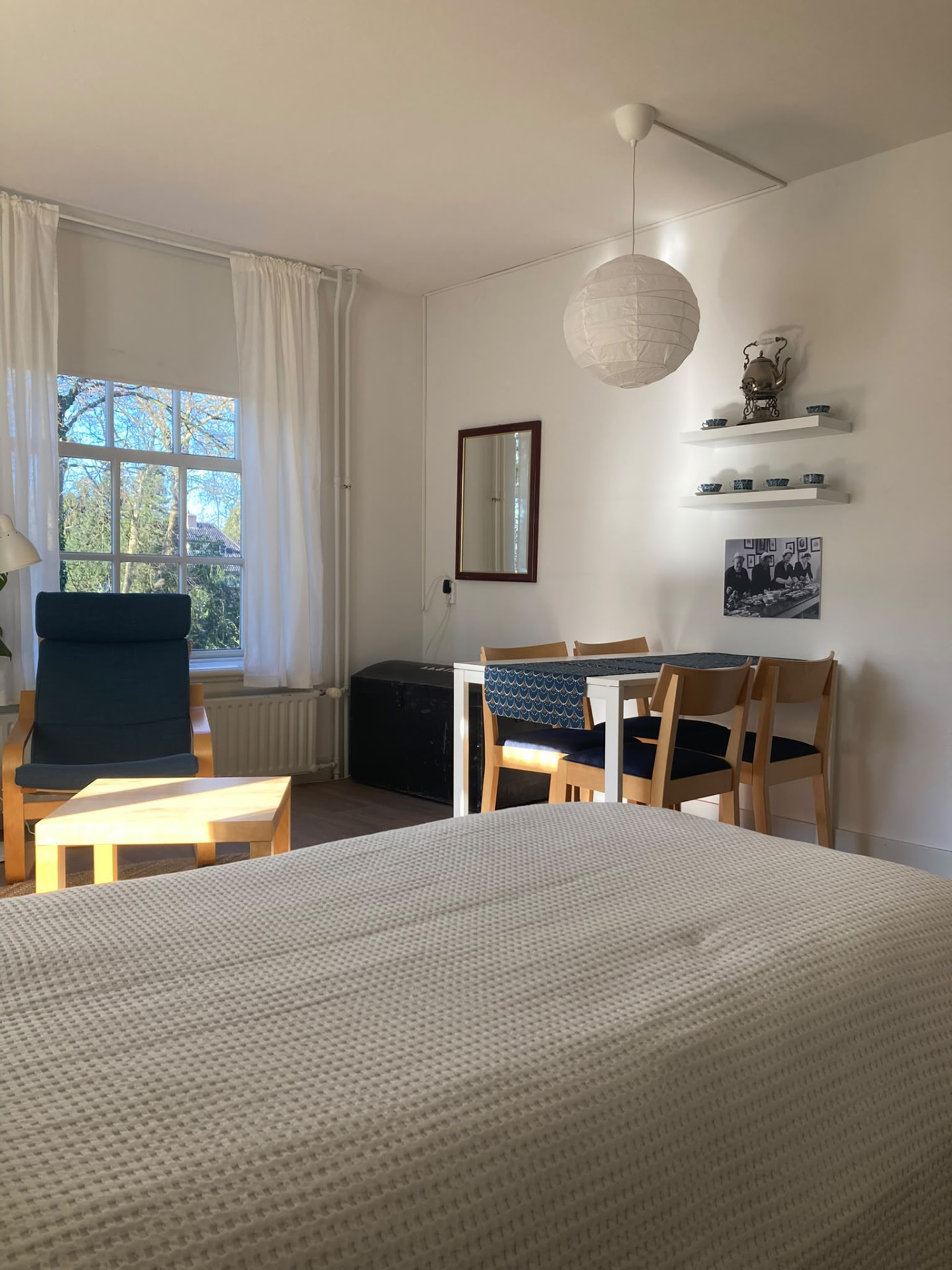 Licht appartement met tweepersoonsbed, fauteuil bij het raam en eettafel met stoelen