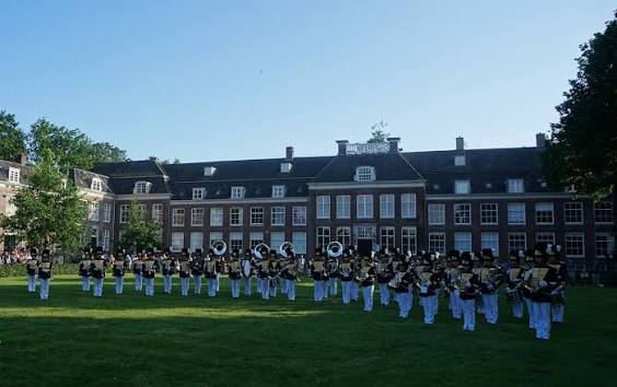Marchingbands in uniform spelen op het gazon van het Zusterplein voor een monumentaal pand
