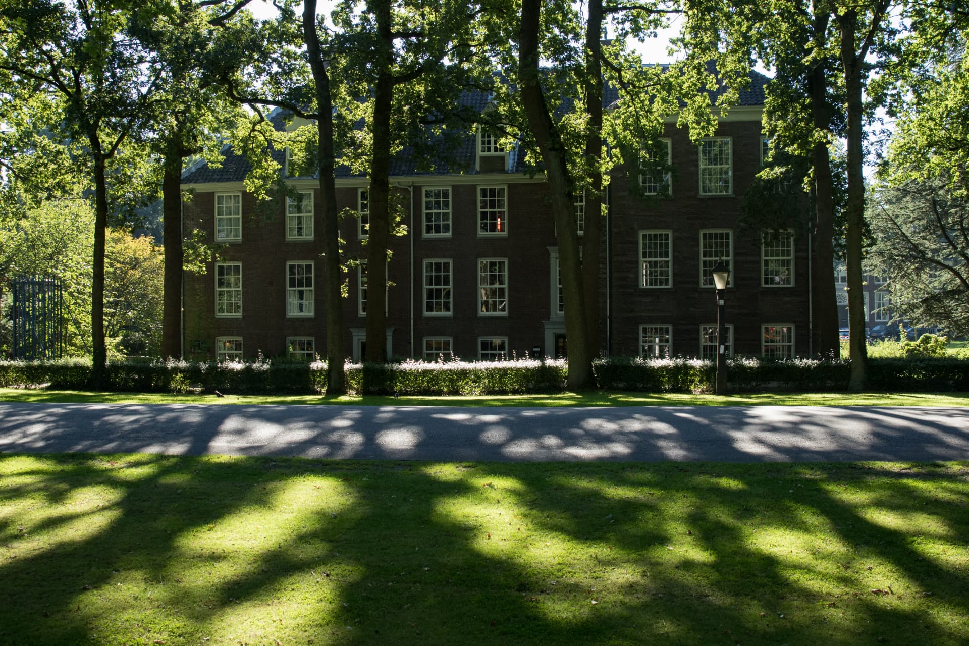 Monumentaal pand aan het plein, omzoomd door hoge bomen en gras